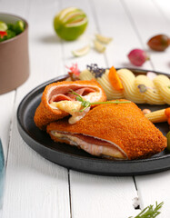 cordon bleu chicken With cheese and herbs, next to mashed potatoes, assortment of side dishes, white wooden background