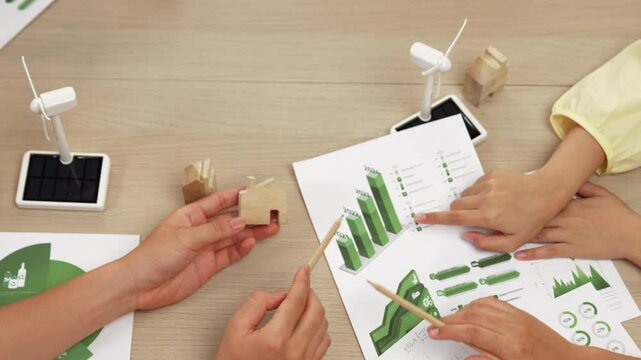 Excellent business people collaborate on eco house project at office with green energy using graph, windmill, home and tree model to decrease carbon footprint, save earth. Focus on hand. Delineation.