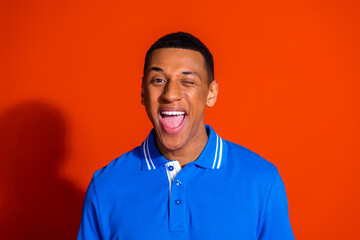 Cheerful young man winking against a vibrant orange background