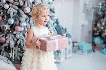 Fototapeta premium Little girl in a festive outfit carefully decorates a stylish Christmas tree.