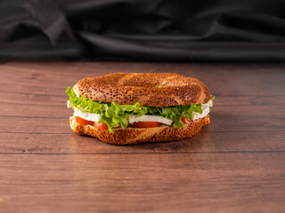 Delicious simit sandwich, close up image of traditional Turkish delicious simit sandwich. Tomatoes, white cheese and lettuce in fresh baked round bagel with sesame seeds on wooden background. © Designerant