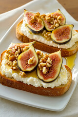 A white plate topped with two slices of bread covered in figs and walnuts