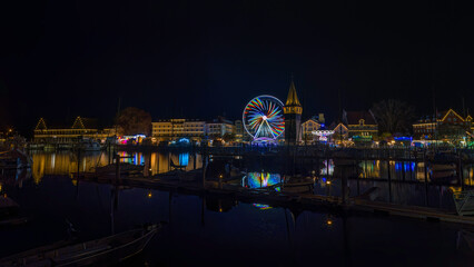 Fototapeta premium Panoramaaufnahme eines Jahrmarkts in Lindau am Hafen, bei Nacht, mit Riesenrad und Kettenkarussell.