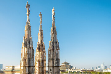 Spires of Gothic cathedral Duomo di Milano with statues and ornate decorations against clear blue sky and modern city skyline, Milan, Lombardia, Italy. Close up