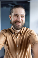A cheerful individual in casual attire capturing a selfie in an office, emphasizing friendly and approachable professionalism.