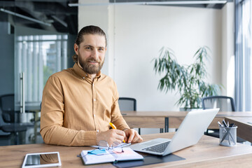 A confident professional sitting at a desk in a bright office, focusing on work using technology and writing tools. The image captures a productive and modern business environment.
