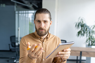 Focused professional man holding a notebook, looking judgmental, inquisitive, and serious, likely...