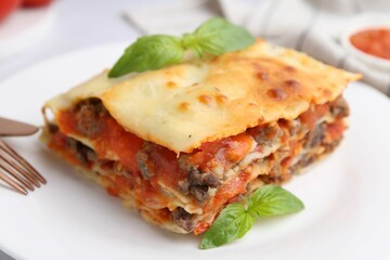 Piece of delicious cooked lasagna with basil on plate, closeup