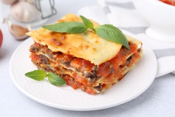 Delicious cooked lasagna with basil on light table, closeup
