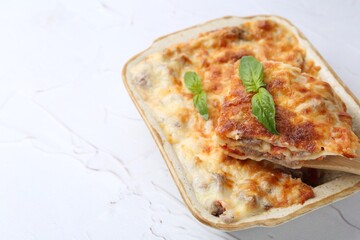 Delicious cooked lasagna with basil in baking dish on white textured table, closeup. Space for text