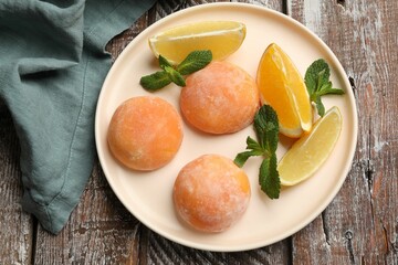 Plate with tasty mochi, cut orange, lemon and mint on wooden table, top view