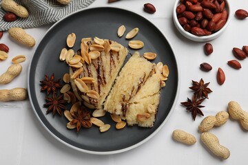Delicious sweet semolina halva with peanuts and spices on white tiled table, flat lay