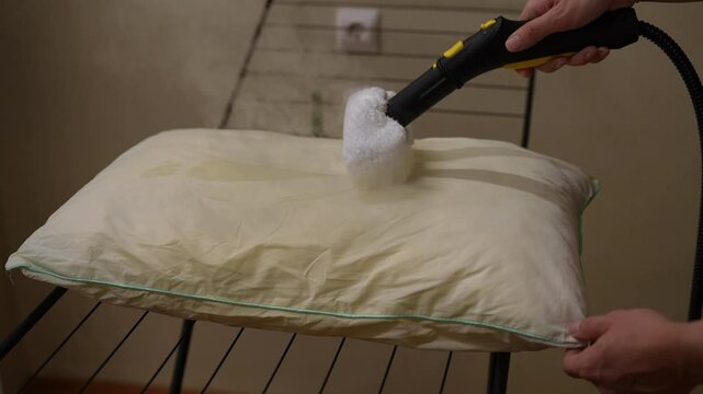 Housekeeper using a steam cleaner to clean pillow, removing dust mites, bed bugs and other allergens, ensuring hygienic and healthy sleeping environment. Concept of easy housekeeping domestic life.