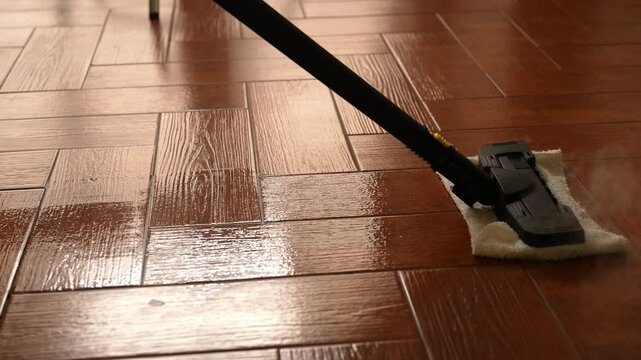 Cleaning company worker steam cleaning wooden floor with steam mop cleaner, making floor shiny and disinfected, removing dirt and dust. Concept of easy housekeeping domestic life, slow motion, closeup