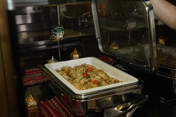 A close-shot of tantalizing tray of seasoned chicken accompanied by colorful vegetables, showcased in a chafing dish, radiating warmth and inviting guests to indulge in a flavorful culinary experience