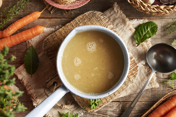 Chicken bone broth in a blue saucepan with fresh vegetables and herbs