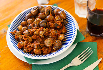 Plate contains dish of Mediterranean cuisine - snails with minced meat and tomato sauce. Gastronourism, national festive Spanish food.