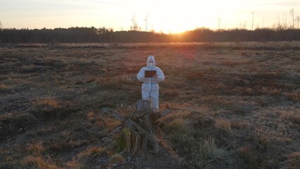Obraz premium Scientist in protective suit on devastated outdoor area with mask and tablet collecting data about contaminated soil after catastrophic event