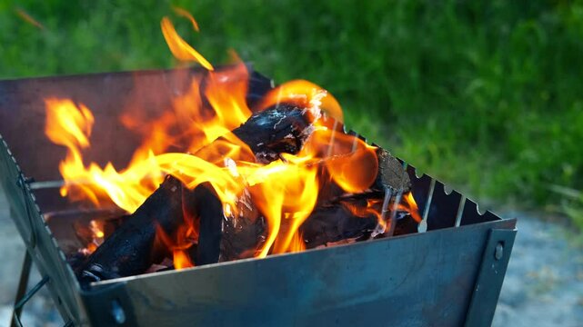 Wood in flame for bbq in field. A view of wood for bbq in the metal box in fire during picnic time in summer.