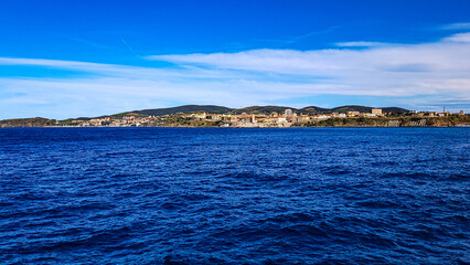 View of the city of Piombino from the Mediterranean Sea. In the foreground - dark blue waves, on the back - a blue sky with white clouds. Tuscany, Italy.