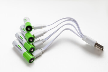Four rechargeable batteries with plugged in USB plugs charging wires, close-up on white background
