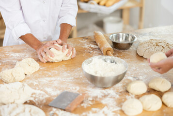 Hands shaping dough in a professional bakery setting, with loaves and tools in the background.