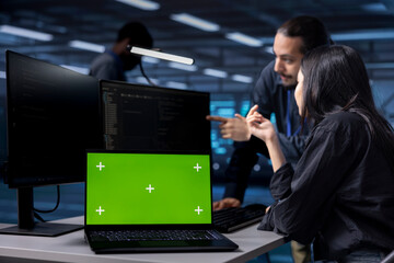 Multiracial team reconfiguring server farm to optimize it for data processing using green screen laptop. Diverse coworkers ensuring data center equipment operates efficiently using mockup notebook