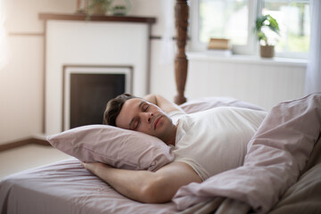 A man peacefully sleeping in a cozy bed with pink sheets and a white t-shirt, natural light...