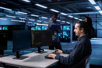 Multiracial team in data center facility running system diagnostic tests on computers. Diverse employees in server farm establishment deploying error checking utilities to mend network issues