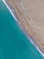 High-angle view of turquoise ocean meeting a beige sandy beach.An aerial shot of a beautiful turquoise ocean meeting a wide stretch of beige sand beach.