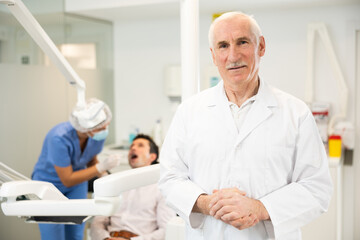 Fototapeta premium Mature man dentist posing while examining patient in dental clinic