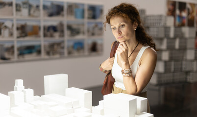 Thoughtful woman in her middle ages gazing at displayed city models in exhibition hall © JackF