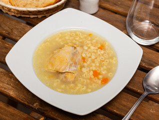 There is plate with hot lunch on table. Soup made from fragrant chicken broth, potato slices, pasta and carrots. View from above