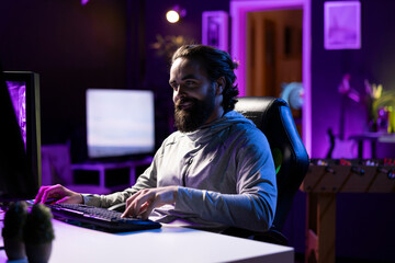 Fototapeta premium Smiling man plays online multiplayer videogame with friends, feeling happy. Cheerful player talking with teammates, enjoying leisure time, controlling character, finishing missions
