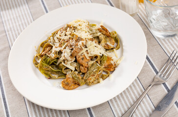 Hearty and simple homemade lunch. Italian past with mushrooms, dish is sprinkled with grated cheese. Cutlery and glass for drinks are prepared for meal.