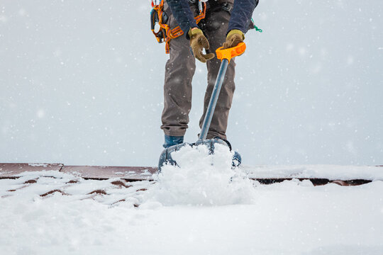 Communal services worker industrial climber removes snow from the building roof in winter. Cleaning city streets, roads and buillding roofs after snow storm in Moscow, Russia.