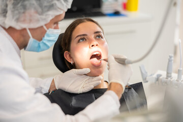 During reception, dental practice, man doctor treats patients girl, improves condition of teeth with help of polymer materials and modern technology