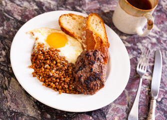 Appetizing roasted beef hamburger cutlet served with lentils and fried egg on platter