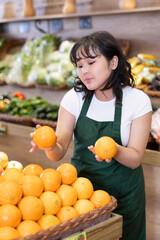 Delighted young saleswoman placing oranges on food stall in large grocery store