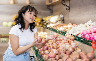 Pleased young woman customer taking fresh onions at the counter in large greengrocery