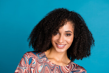 Smiling young woman with curly black hair posing against a vibrant blue background, highlighting her colorful t-shirt