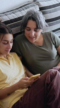Mother and daughter sharing quality time watching smartphone. Hispanic, single family