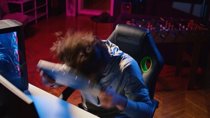 Angry man playing videogames at home, smashing head on keyboard after being defeated by enemies. Competitive pro gamer raging after failing to win online multiplayer esports match, feeling annoyed © DC Studio