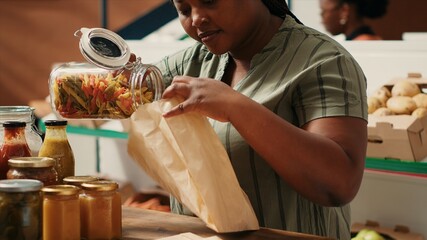 African american woman pours pasta in biodegradable bag to shop for bulk items at local farmers market. Client choosing eco gluten free products, supporting small business and vegan lifestyle.