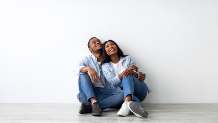 Decoration and furniture concept. Happy african american couple sitting on floor in new appartment, embracing, planning interior and looking up at empty space