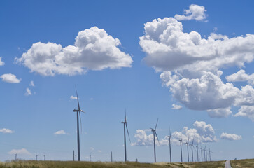 Windmills generating electrical energy on the side of a road. Blue sky with cotton clouds, rural landscape