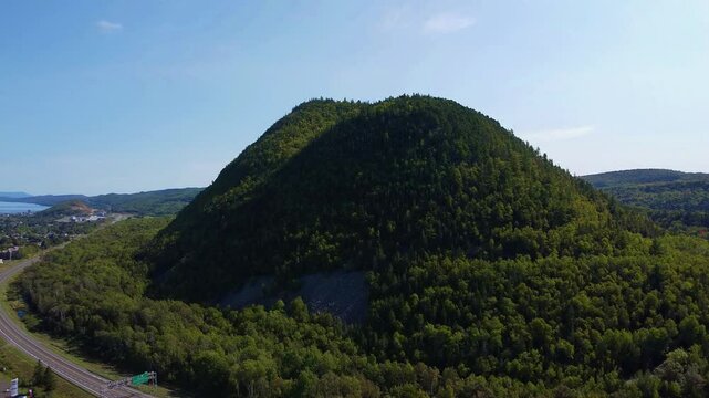 Aerial view of Sugarloaf Mountain, an ancient volcano located in Atholville, New Brunswick, with Chaleur Bay and the city of Campbellton in the background under a blue sky.