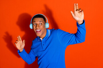 Young man enjoying music with headphones against orange background in blue shirt