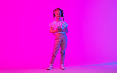 A Caucasian preteen girl stands confidently in a vibrant neon light environment. She is dressed stylishly and wears headphones, immersed in her music while showcasing her unique personality.