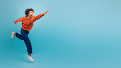 A young African American man with curly hair is energetically running and pointing at copy space,...